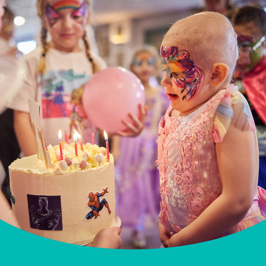 Wish child, Ryleigh with her face painted, blowing out candles on her birthday cake.